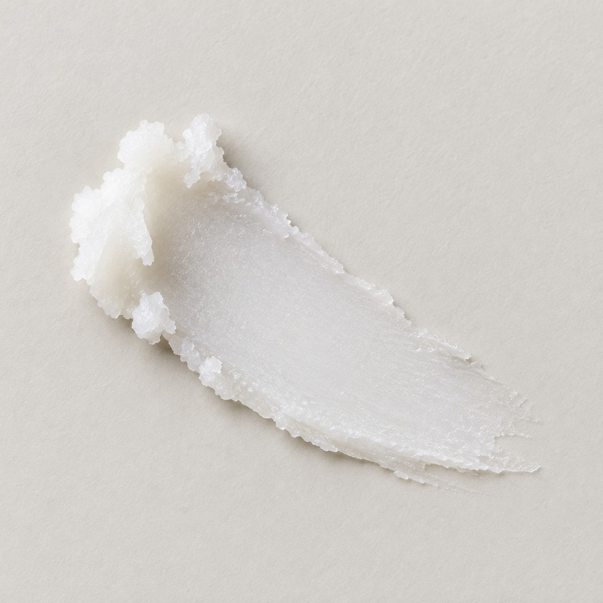 A smear of white, luxury lip butter on a light beige background.