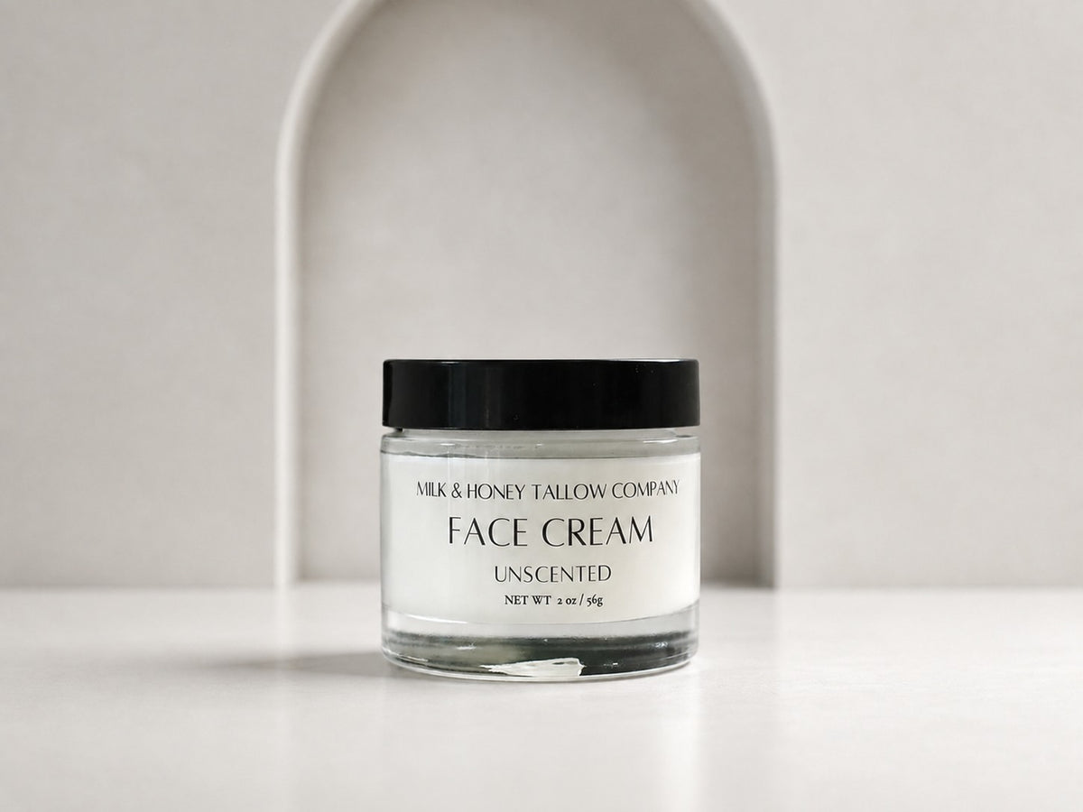 A clear glass jar of Milk & Honey Tallow Company Face Cream, Unscented, with a black lid and white label, set against a minimalist white background with a subtle arch.