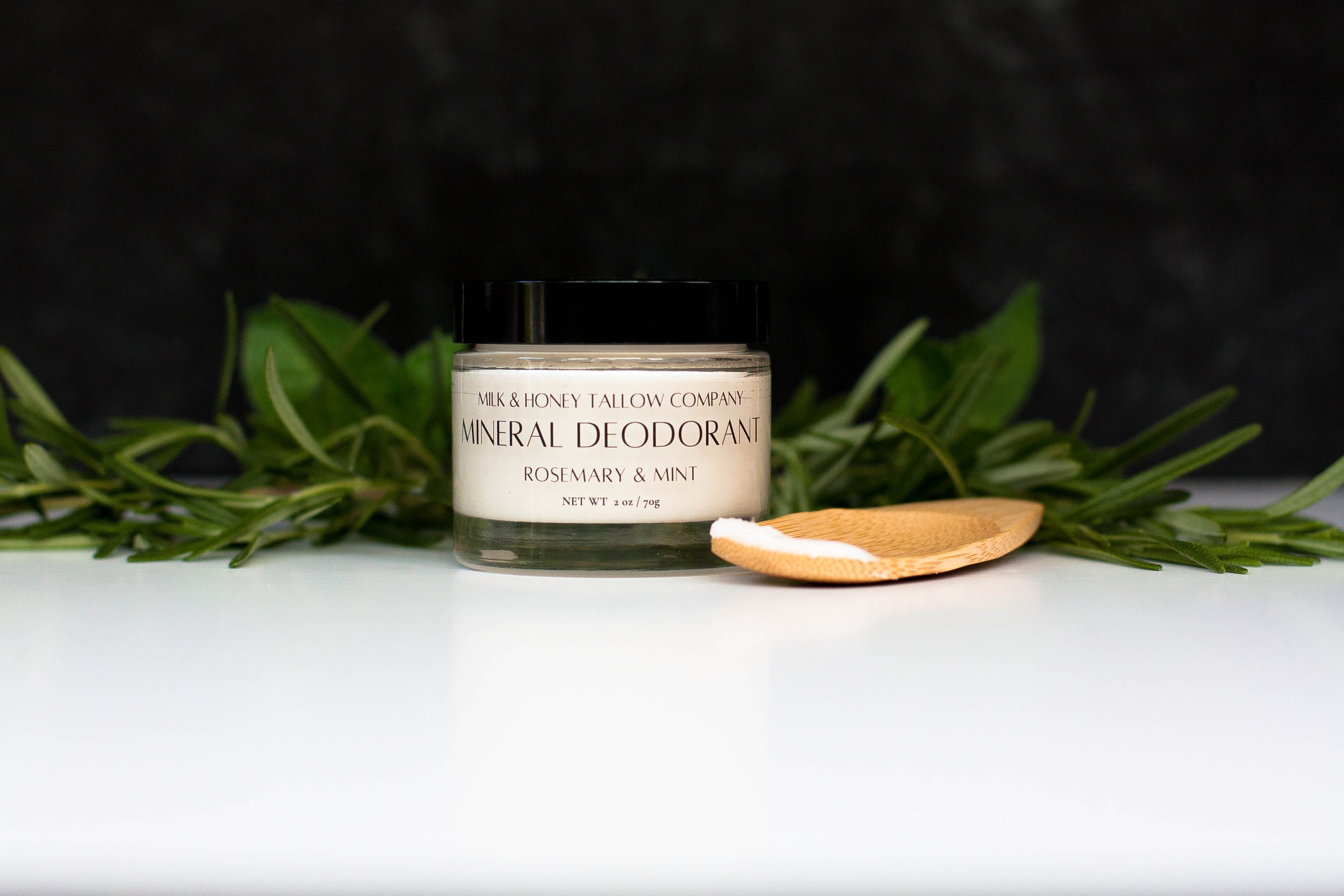 Jar of mineral deodorant with rosemary and mint on a white surface with greenery.