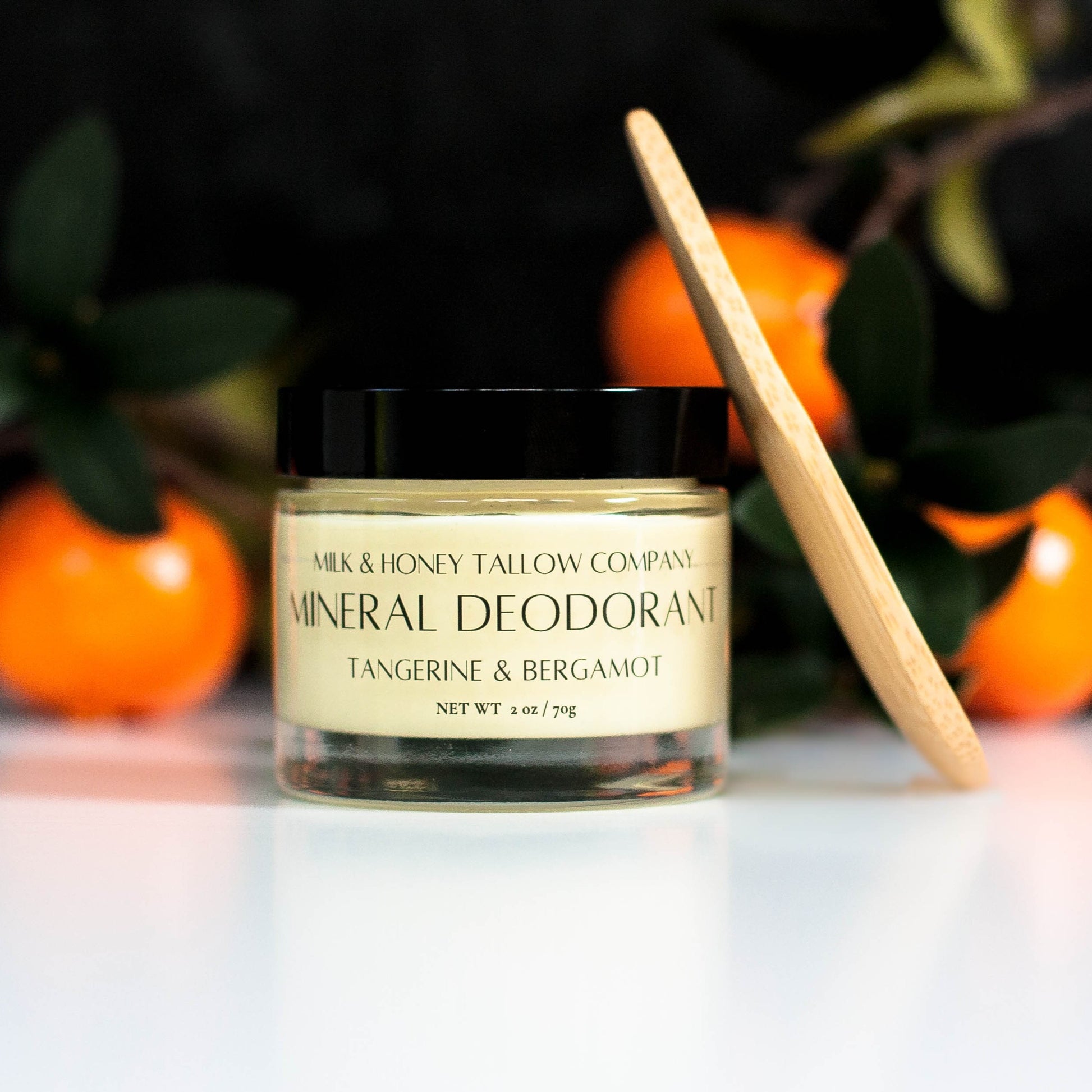 Jar of Tangerine and Bergamot Mineral Deodorant with a wooden applicator against a blurred background with tangerines.