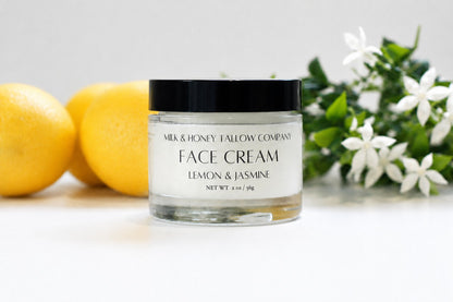 A jar of Milk & Honey Fallow Company Face Cream in Lemon & Jasmine scent, styled with fresh lemons and white flowers on a clean white background.