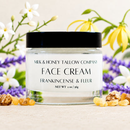 glass jar of frankincense and fleur tallow face cream with botanicals of ylang ylang, jasmine, lavender, and frankincense displayed around it