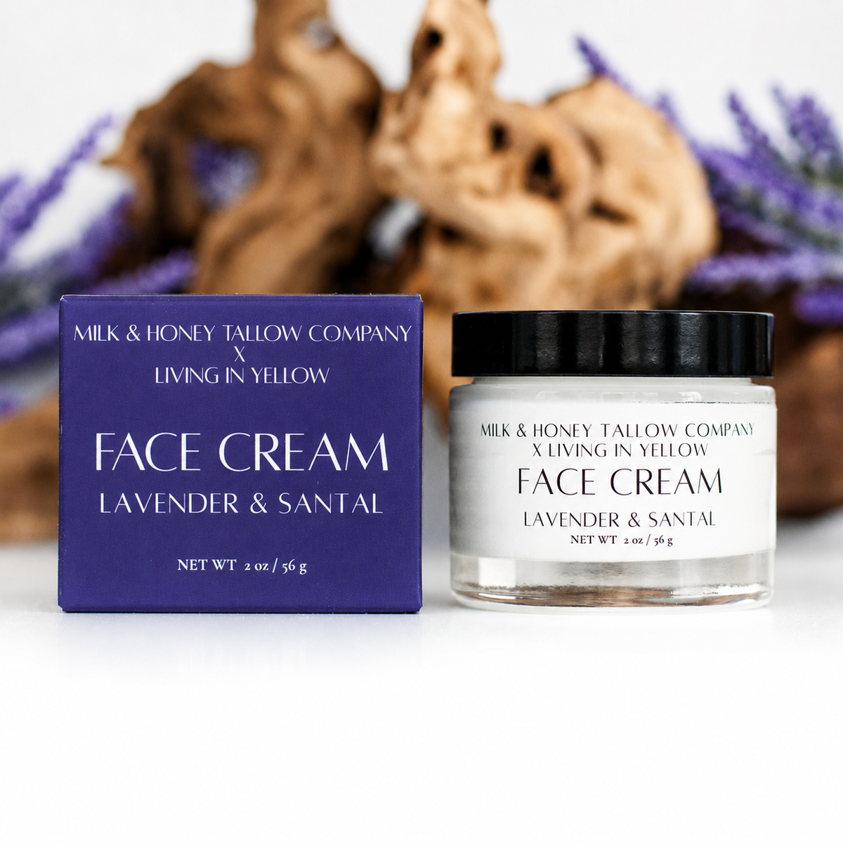 A jar of lavender and santal face cream and its matching purple box on a white surface, with a blurred natural wood and lavender background. The box and jar label read 'MILK & HONEY TALLOW COMPANY x LIVING IN YELLOW FACE CREAM LAVENDER & SANTAL'.