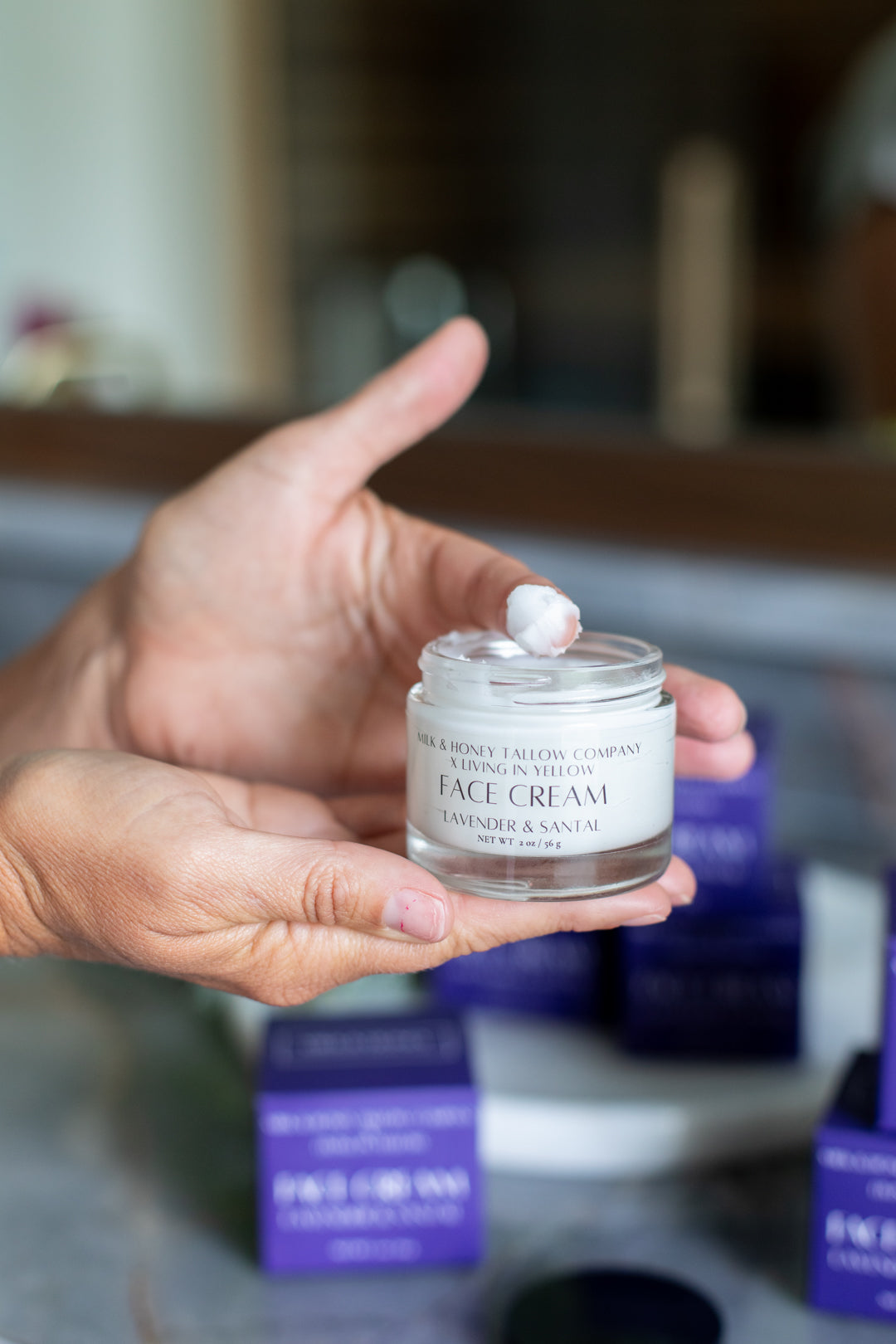 Hand holding a jar of lavender & santal luxury face cream with blurred background