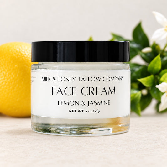 Glass jar of lemon and jasmine tallow face cream with lemons and jasmine flowers in the background
