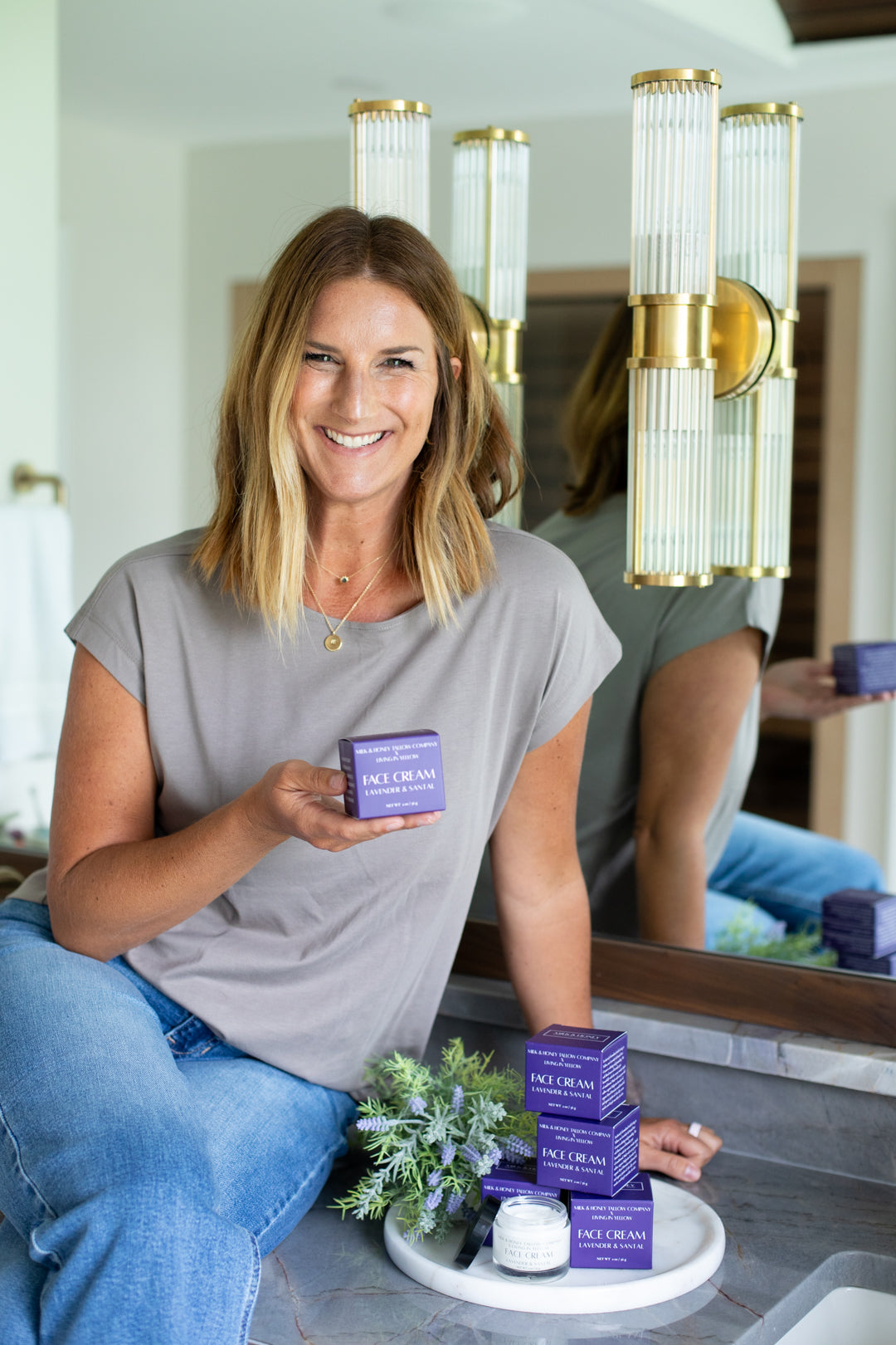 Woman holding a lavender & santal face cream in a purple skincare product box in a modern interior setting