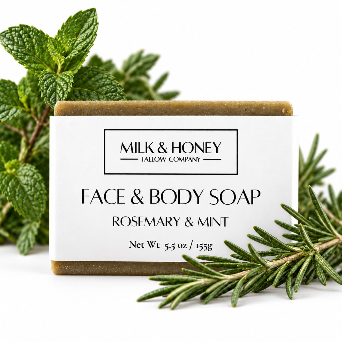 Rectangular bar of Rosemary & Mint Face & Body Bar Soap. Fresh peppermint leaves and rosemary sprigs are decoratively placed around the bar on a white background.