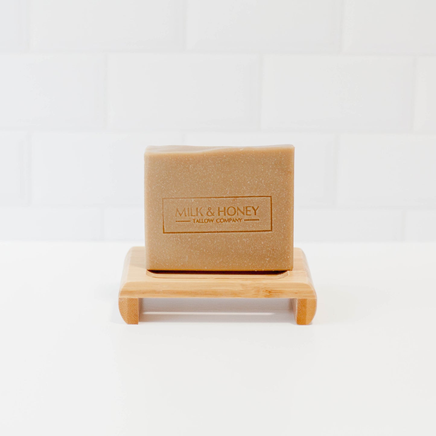 Bamboo soap stand with bar of soap on white counter with white tile backsplash