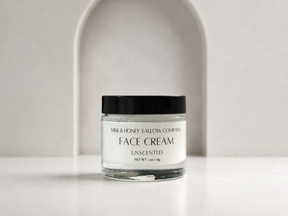 A clear glass jar of Milk & Honey Tallow Company Face Cream, Unscented, with a black lid and white label, set against a minimalist white background with a subtle arch.
