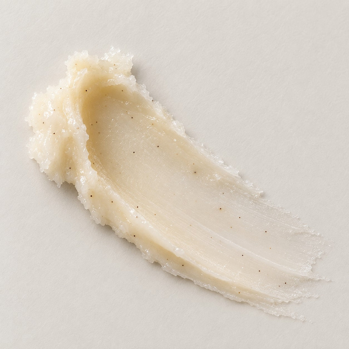 A thick, creamy smear of Vanilla Bean Lip Butter on a light beige background, showing a luxury texture with tiny dark vanilla bean seed pods.