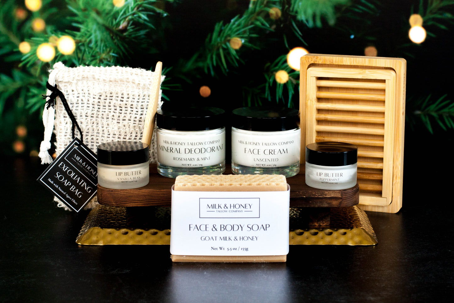 Collection of natural tallow skincare products including jars and a bar of soap on a dark surface with a blurred Christmas tree background.