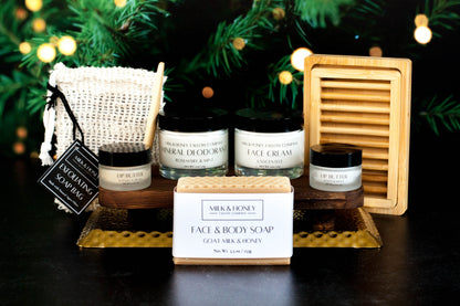 Collection of natural tallow skincare products including jars and a bar of soap on a dark surface with a blurred Christmas tree background.
