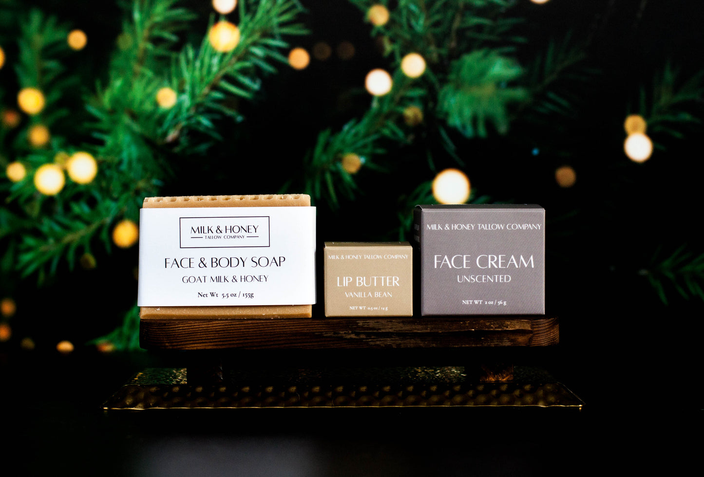 Milk & Honey natural tallow skincare products on a wooden stand with Christmas lights and greenery in the background