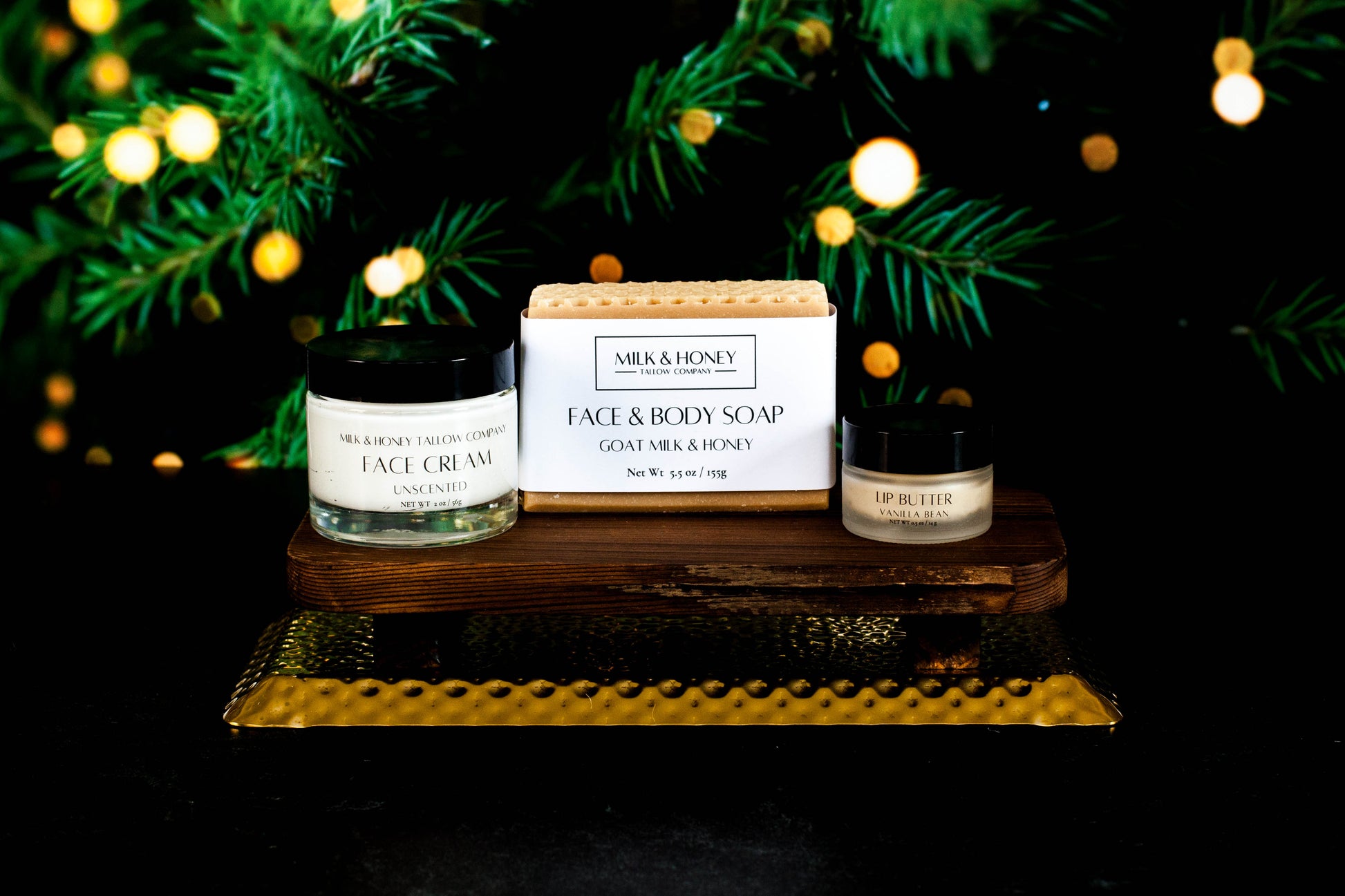 Milk & Honey Tallow skincare products on a wooden stand with Christmas tree and lights in the background